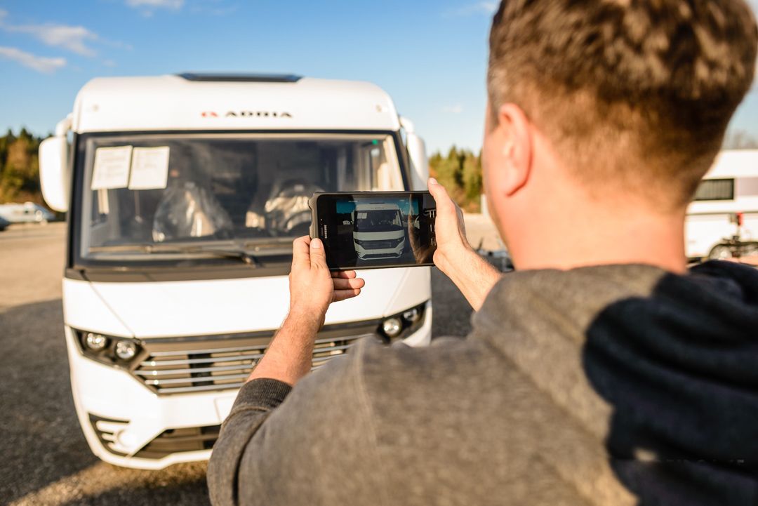 Moški s tablico fotografira avtodom na parkirišču